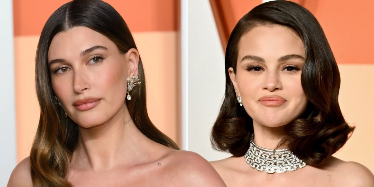 Side-by-side portraits of Hailey Bieber and Selena Gomez against warm, peach-toned backgrounds. Hailey Bieber is shown on the left wearing a strapless gown with long, straight brown hair parted in the center and statement earrings. Selena Gomez appears on the right wearing a strapless gown, a diamond necklace, and softly styled dark hair in vintage-inspired waves. Both are photographed from the shoulders up with neutral expressions under soft, even lighting.